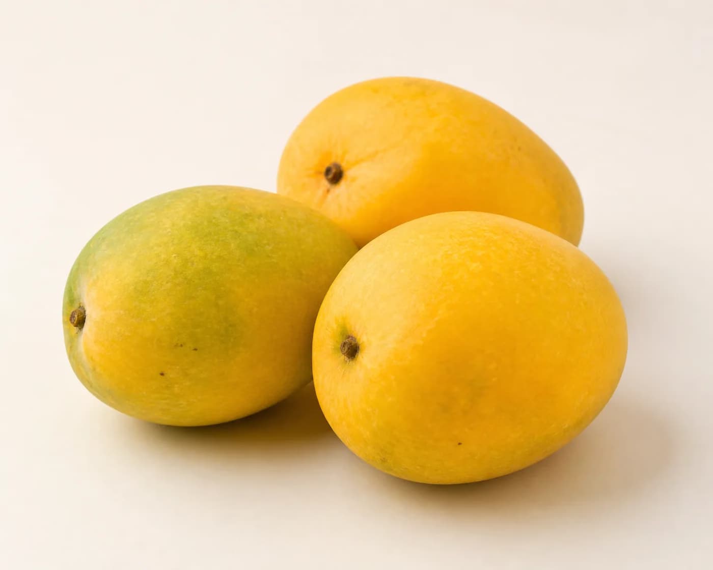 Fresh Mallika Mango arranged on a warm off-white surface.